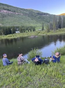 Students sitting in the grass in front of a pond over looking a beaver lodge